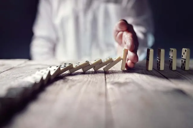 Hand stopping a line of falling dominoes
